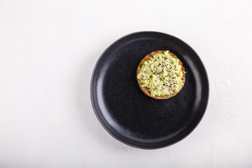 Whole grain bread avocado sandwich seasoned with black and white sesame on black plate.