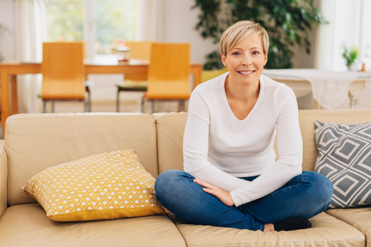 Healthy relaxed woman sitting cross-legged on sofa
