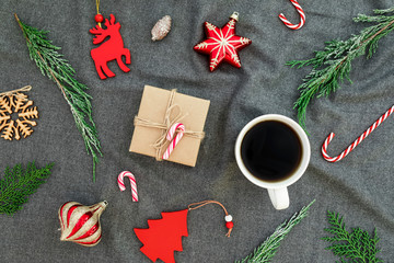 Christmas tree decorations, evergreen branches, mug of coffee and gift box on gray plaid. Flat lay, top view. Christmas, New Year, winter composition.