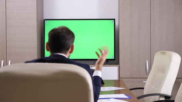 Back Of Businessman Head Talking To A Green Screen Mock-up TV. Dolly Slider 4K Footage