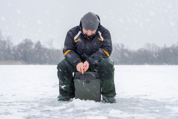 Fototapeta na wymiar Winter fishing concept. Fisherman in action, catching fish from ice in snowy weather.