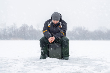Fototapeta na wymiar Winter fishing concept. Fisherman in action, catching fish from ice in snowy weather.