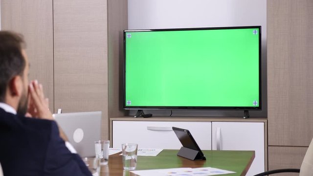 Businessman in conference room talking with a green screen mock-up TV. Replace the green screen with your own clip. Dolly slider 4K footage
