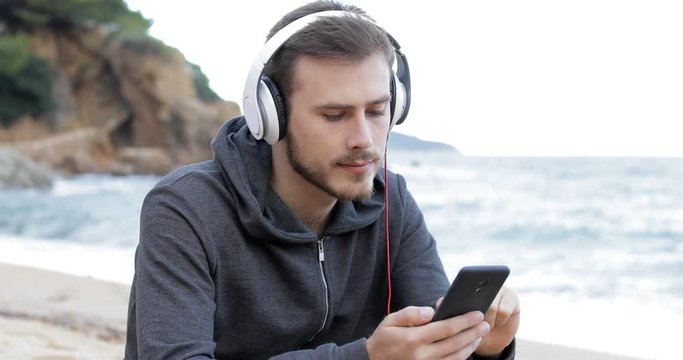 Teenage boy listening to music from a smart phone on the beach and watch the sea