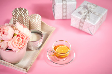 Fototapeta na wymiar peonies, candles on a wooden tray, tea and gifts on a light pink background