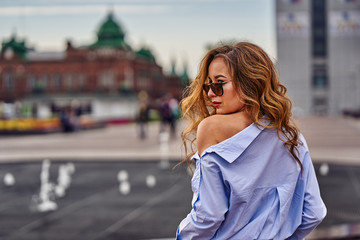 Young beautiful woman with long brown hair in sunglasses on a walk on a cloudy day.