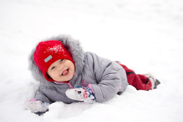 Fototapeta na wymiar Child lies in the snow and shows tongue.