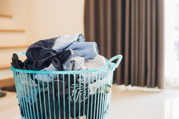 Clothes in a laundry plastic basket on tiled floor on the background of curtain and staircase.