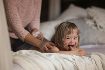 mom massage to child with Down syndrome on bed