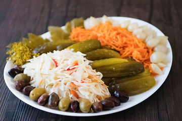 Assorted pickled and fermented vegetables in a white plate on a brown wooden background.