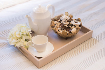 Morning lifestyle. A wooden tray with a cup of tea and dry flower on the bed.
