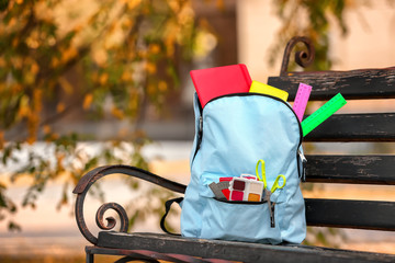Color rucksack with school stationery on bench outdoors