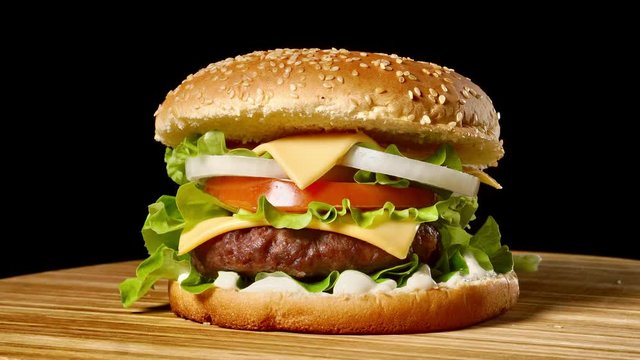 Closeup of home made beef burgers with lettuce and mayonnaise served on little wooden cutting board. Dark background