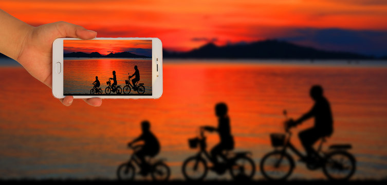  Tourist taking a picture of blur image of silhouette family  riding bicycle on sunset
