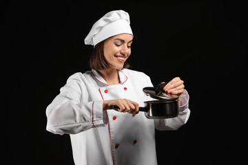 Young female chef with pot on dark background