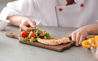 Young female chef putting tasty dish onto wooden board on kitchen table, closeup