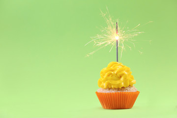 Tasty cupcake with sparkler on color background