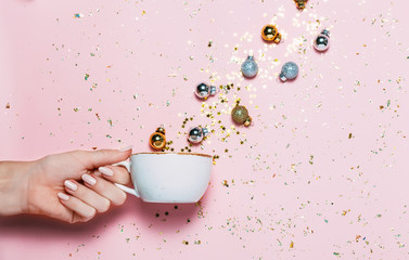 Minimalistic Christmas concept. Woman's hand holding cup with Christmas decorations in cup on pink background.