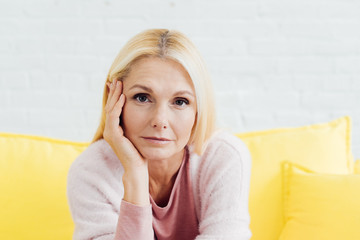 close up of beautiful blonde mature woman sitting on bright yellow sofa