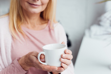 close up of mature blonde woman holding white coffee cup