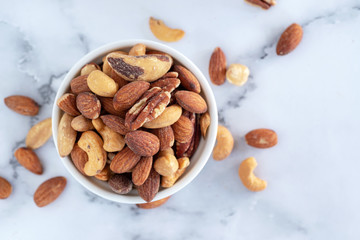 roasted mixed nuts in white ceramic bowl on barble table background.
