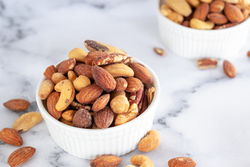 roasted mixed nuts in white ceramic bowl on barble table background.