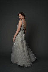 Fototapeta premium full length portrait of brunette girl wearing long silver ball gown. standing pose on grey studio background.