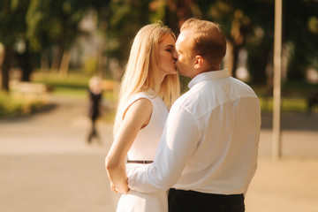 Young beautiful couple husband in a white shirt and a woman in a dress walking around the park in summer time