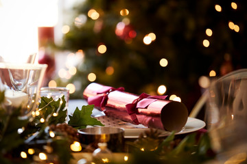 Close up of Christmas table setting with a Christmas cracker arranged on a plate and Christmas tree...