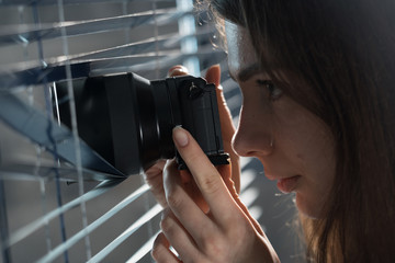 Young woman Paparazzi take a photo suspiciously from around a blinds  while using a camera. GDPR...