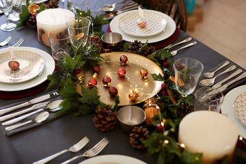 Christmas table setting with bauble name card holders arranged on plates, golden plate centrepiece with baubles, and green and red table decorations, elevated view