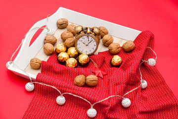 Wooden tray on a red background with nuts lying on a red napkin. The scenery for the New Year's Eve. romantic setting with a candle.