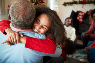 Granddaughter Giving Grandfather Hug As Multi Generation Family Celebrate Christmas At Home - Powered by Adobe