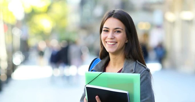 Portrait of a happy student posing holding folders and looking at camera in the street