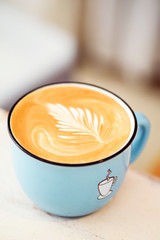 A cappuccino mug with a pattern on the foam. Morning drink in a beautiful blue cup on a light background