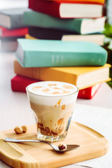 A coffee drink with caramel and pattern on the foam. Morning drink in a rocks glass with hazelnut on a wooden plank with book background