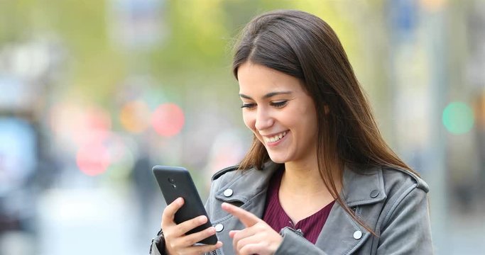 Happy teen browsing on line smart phone content in the street with a green background