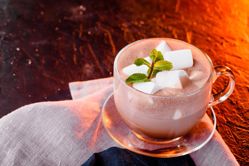 Hot chocolate with marshmallows in a glass cup with mint. Cocoa. sunset orange light