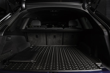 The big black empty trunk of SUV car with rubber mat and with leather folder on the floor  Open...