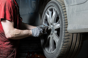 A mechanic in the service center checks the suspension of the dirty car. Performs seasonal wheel replacement.