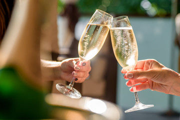 two girls clink glasses of champagne on a beautiful summer terrace. sparkling champagne glasses - obrazy, fototapety, plakaty