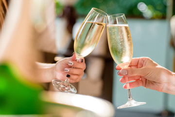 two girls clink glasses of champagne on a beautiful summer terrace. sparkling champagne glasses