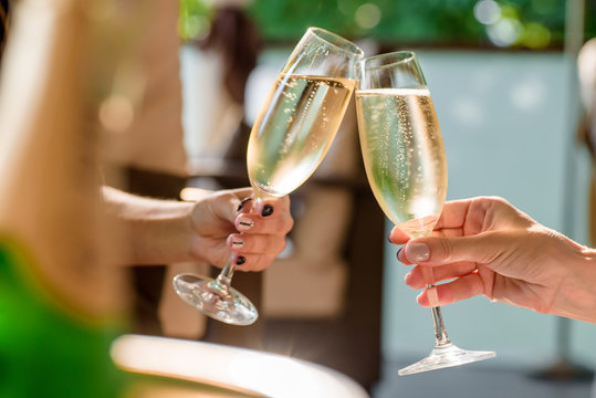 two girls clink glasses of champagne on a beautiful summer terrace. sparkling champagne glasses
