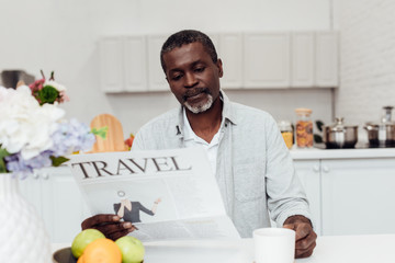 african american man sitting at table and reading travel newspaper at kitchen