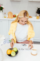 Obraz na płótnie Canvas attractive blonde mature woman reading travel newspaper at kitchen