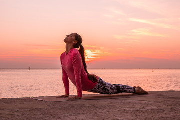 Young beautiful woman practicing Yoga by the sea at sunset