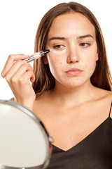 young beautiful girl applying concealer under her eyes on white background