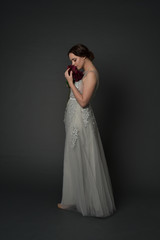 full length portrait of brunette  girl wearing long silver ball gown. standing pose on grey studio background.