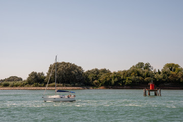 Sailing boat in navigation with wooded coastline, Adriatic Sea, Veneto, Italy
