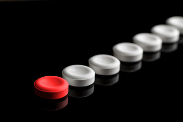 Behind the red pill are lined up white pills. One red and many white pills on a black background....